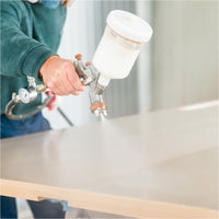 Spritzauftrag von OLI-AQUA NORDIC Rohholzeffektlack mit einer Lackierpistole auf eine Holzplatte