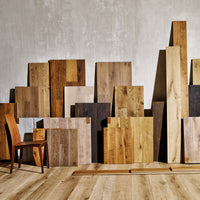 Verschiedene Holz- und Parkettmuster vor einer Betonwand als Inspiration für farbige Holzoberflächen.