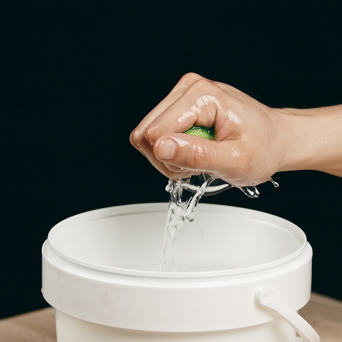 Ein mit verdünntem OLI NATURA® PreOilCleaner angefeuchteter Schwamm wird über einem Eimer ausgewrungen